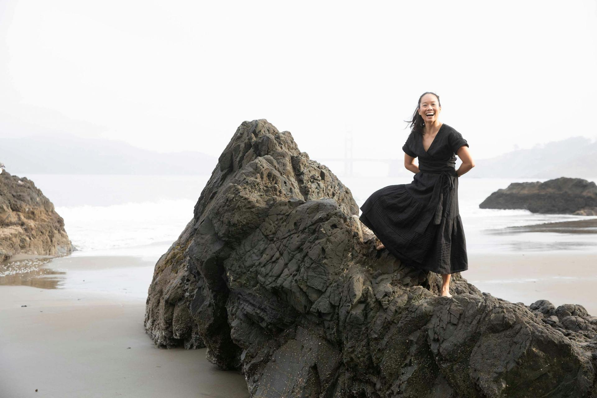 Bonnie Tsui wears a dark outfit and sits on a rock