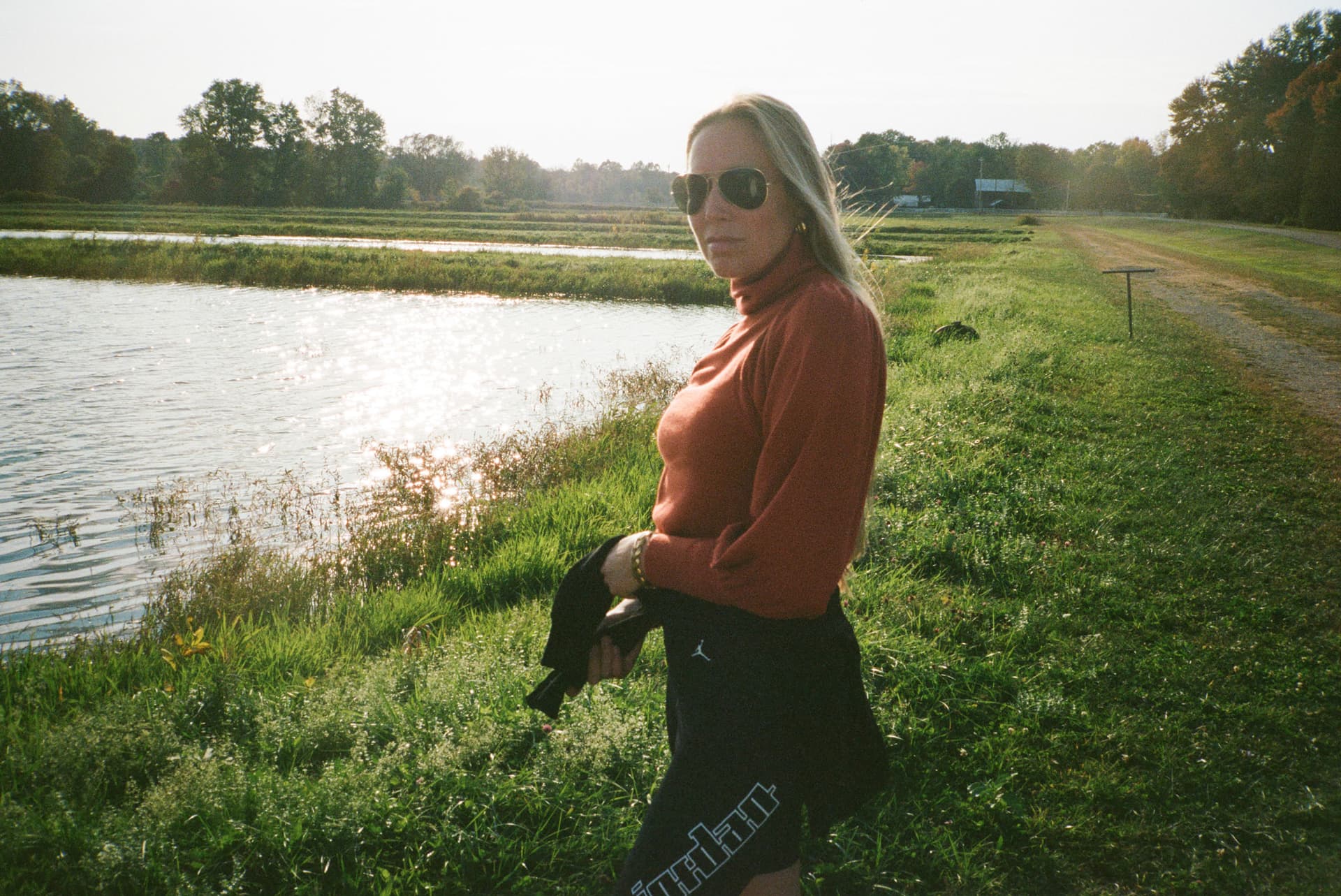 A woman wearing an orange sweater stands next to a pond