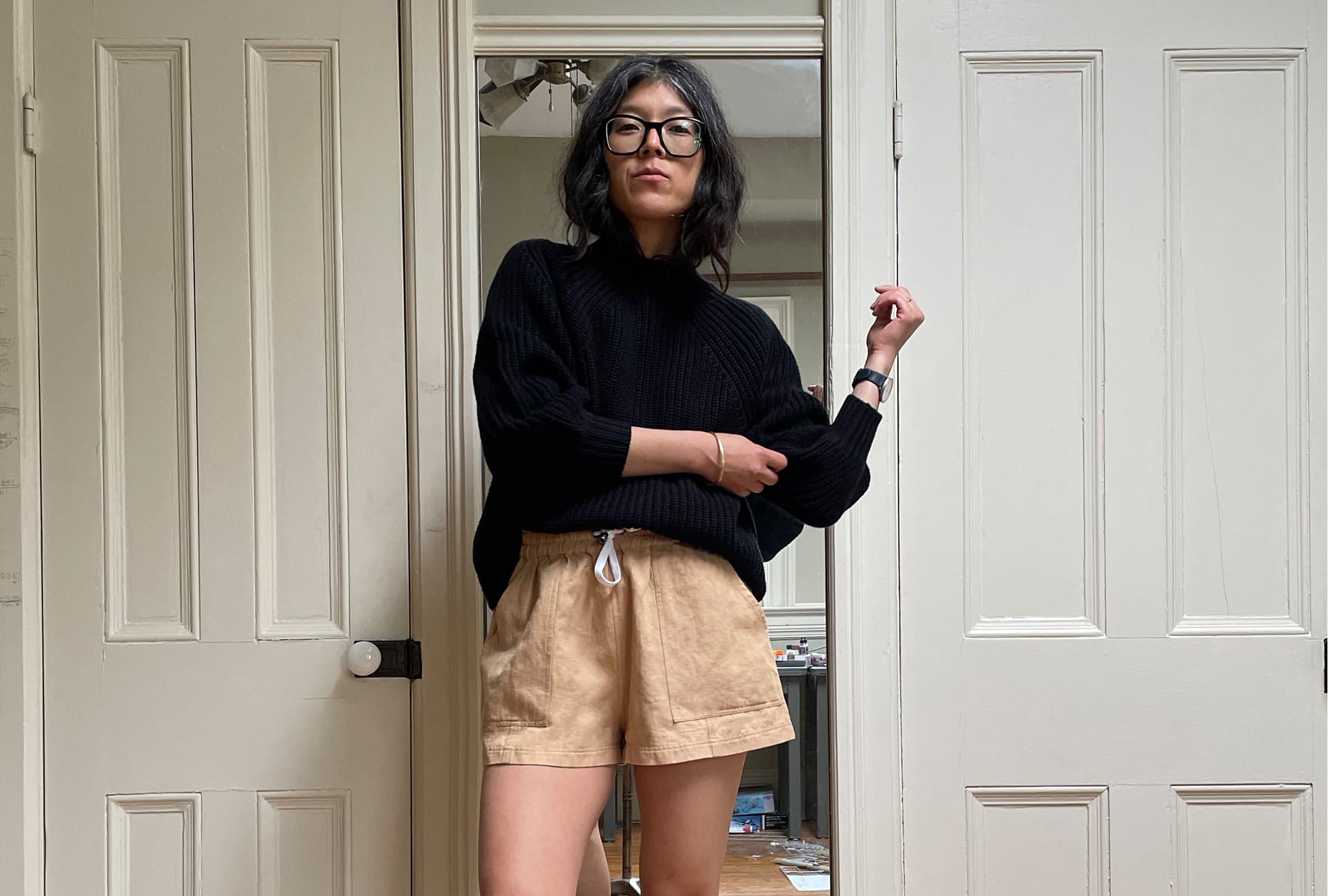 Erica Kim wears a black top, light shorts, and stands in a doorway.