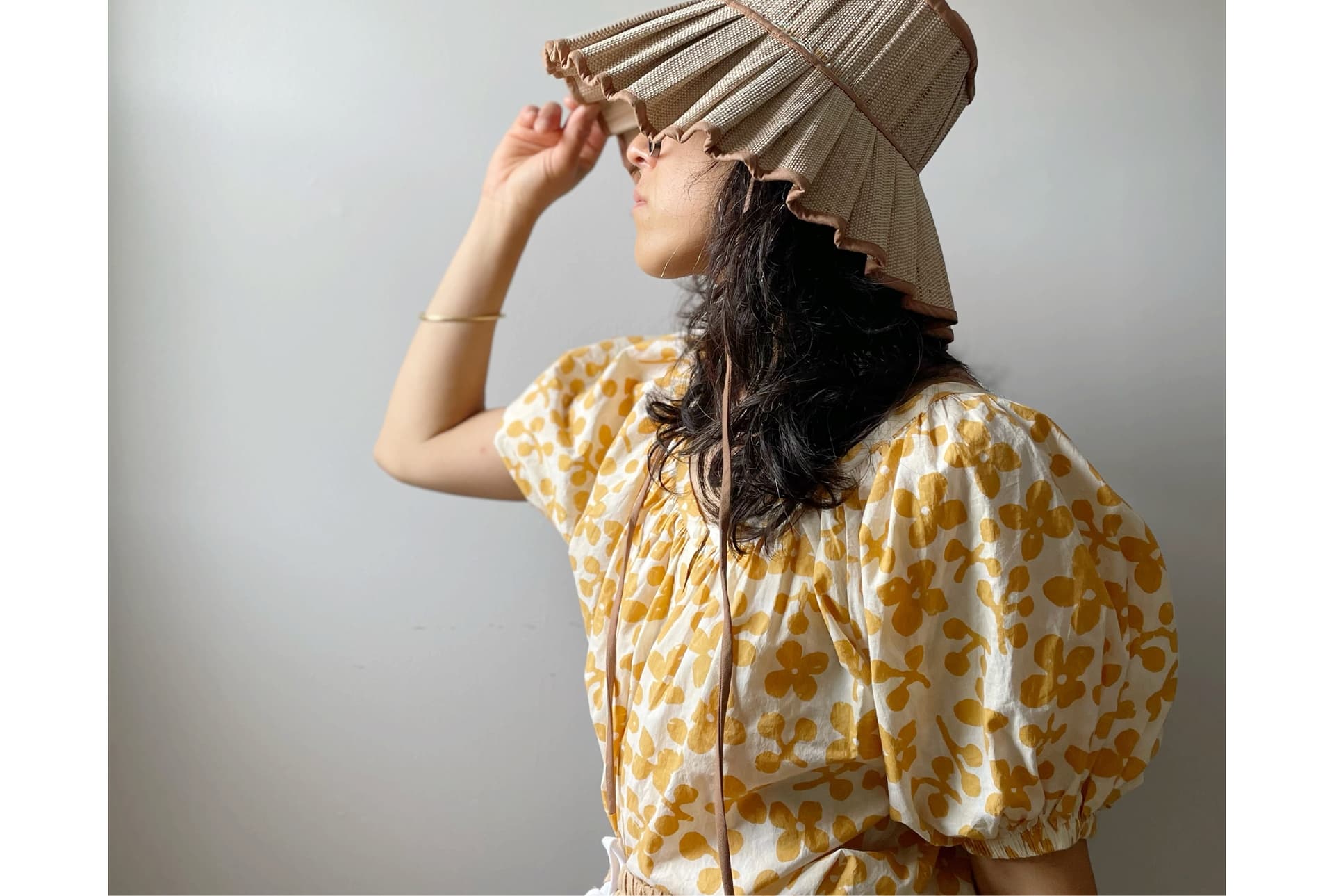 Erica Kim wears a yellow top, light colored hat, and stands in front of a plain wall