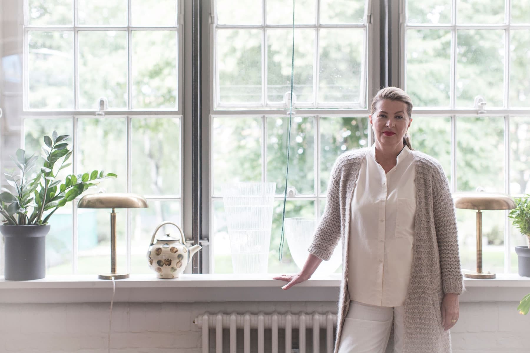 Ilse Crawford wears a light colored outfit and stands in front of a well lit window