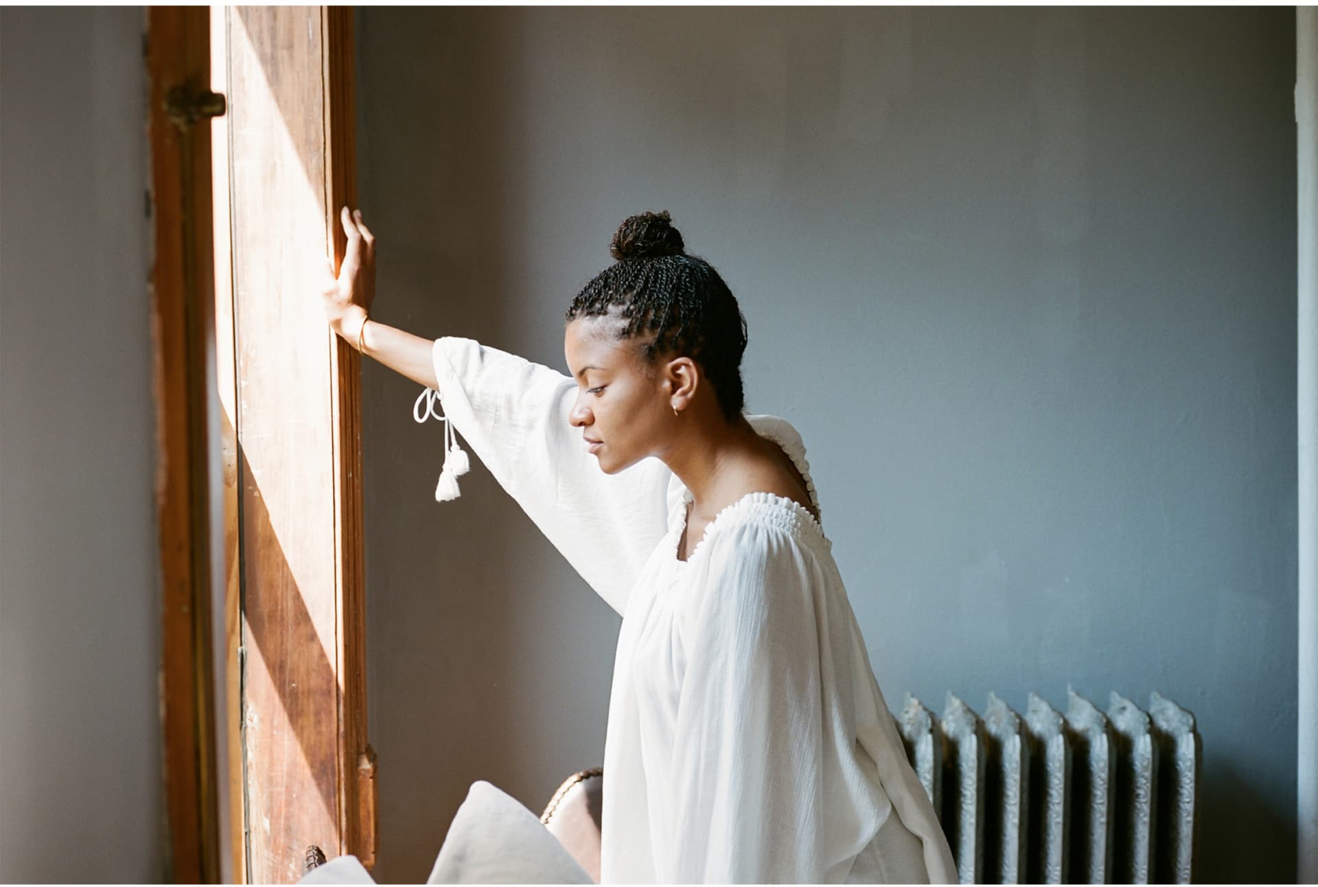 Kai Avent-deLeon wears all white and stands while looking out of a window.