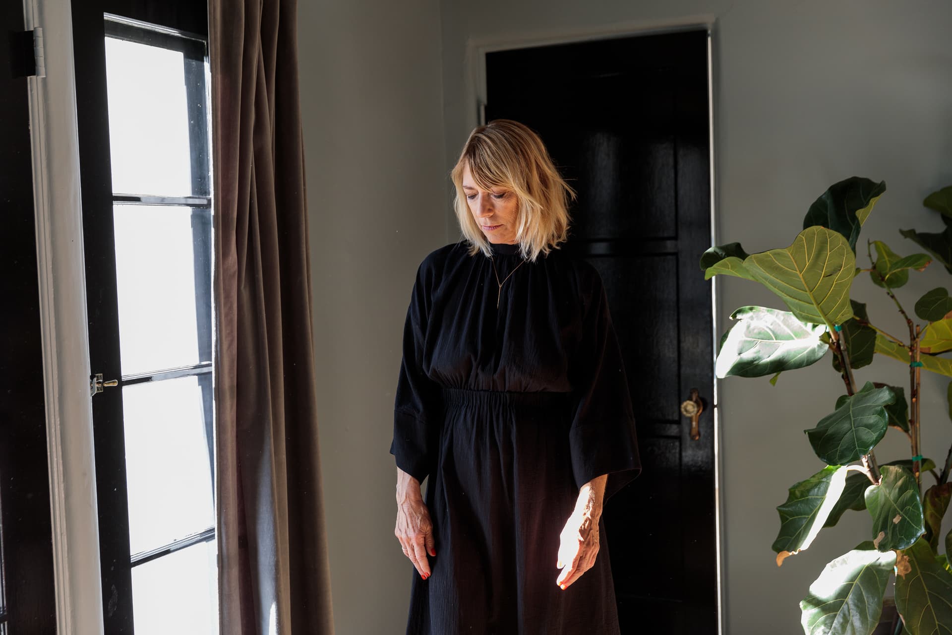Kim Gordon stands in all black looking out a bright window