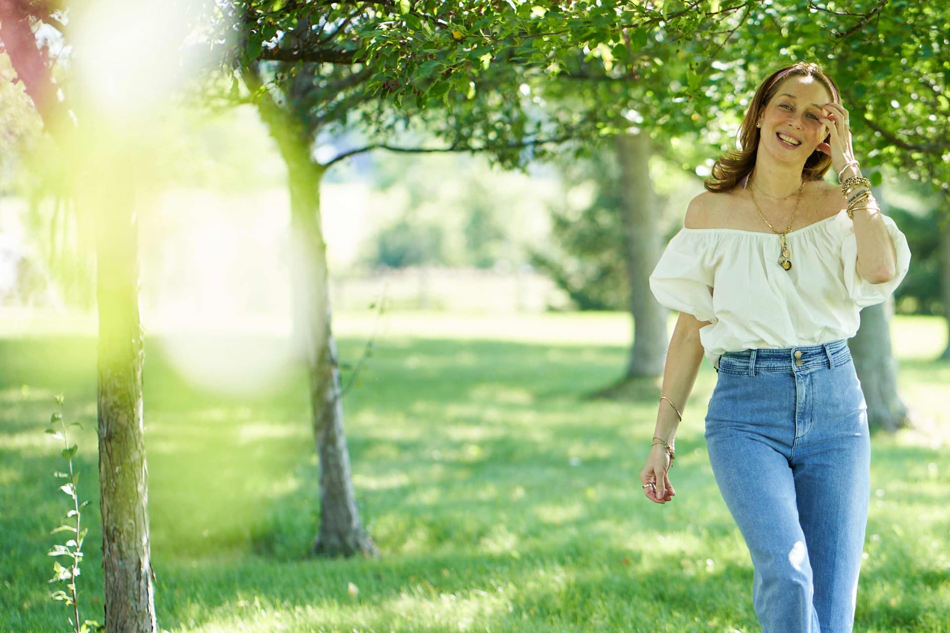 Tata Harper wears jeans and a white blouse and stands outside