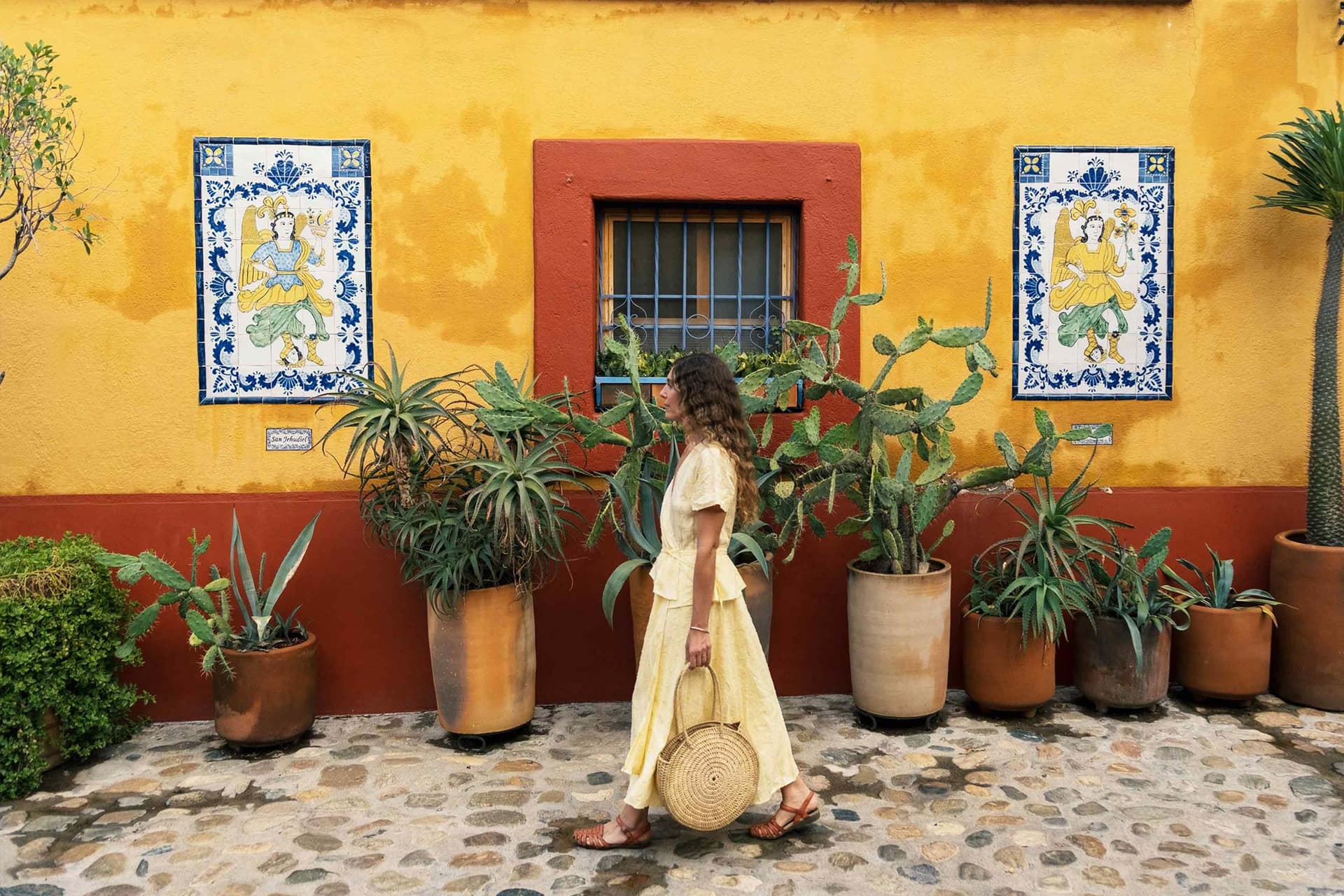 Vera Claire wears a yellow dress and walks while holding a handbag