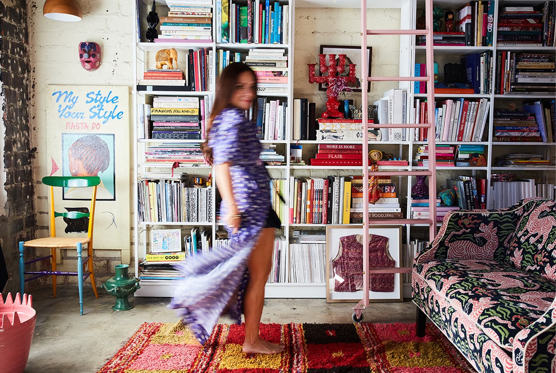 A woman wearing a dress stands in front of books