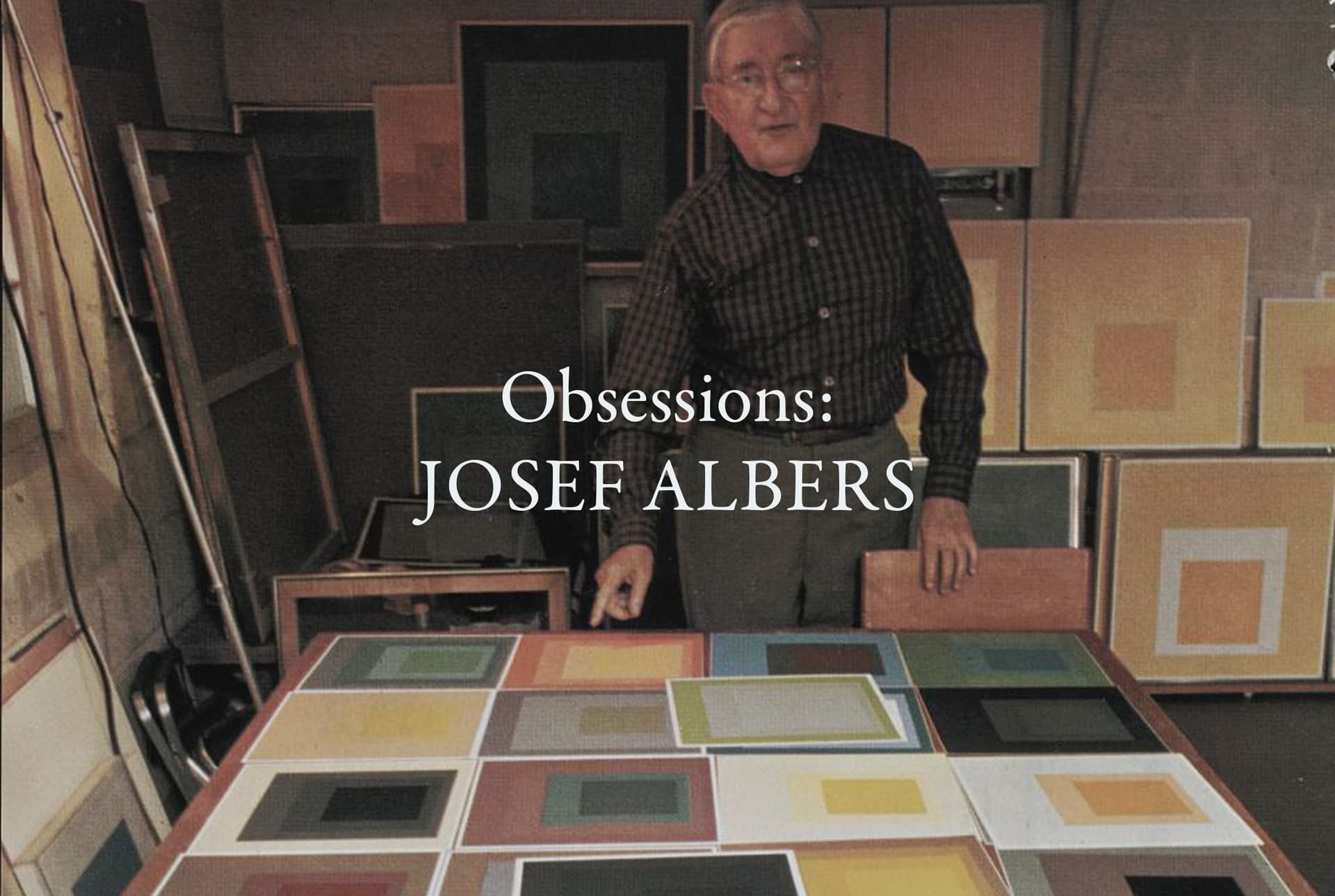 A man wearing a dark outfit stands surrounded by his art