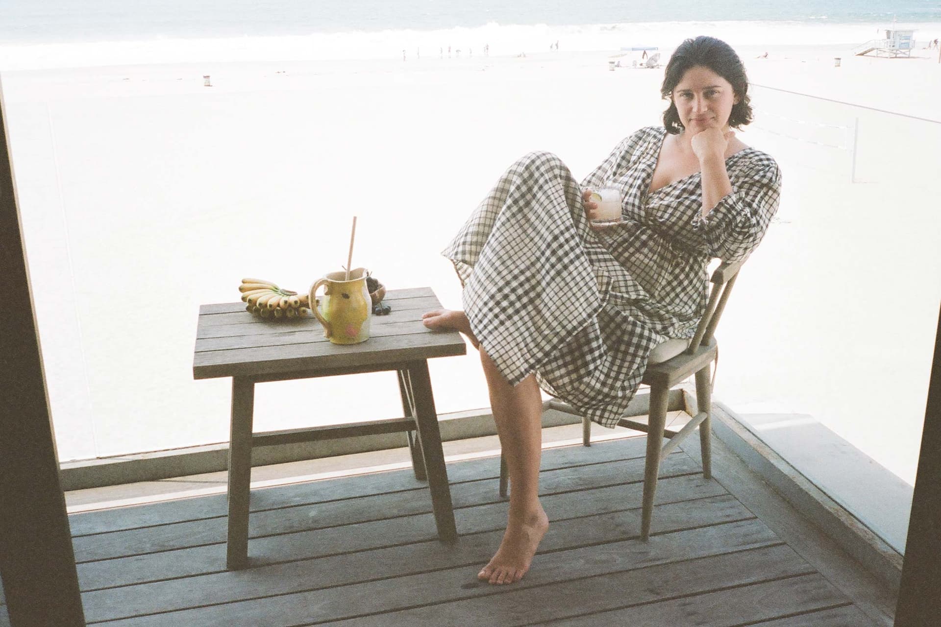 A woman wearing a printed dress sits on a chair outside.