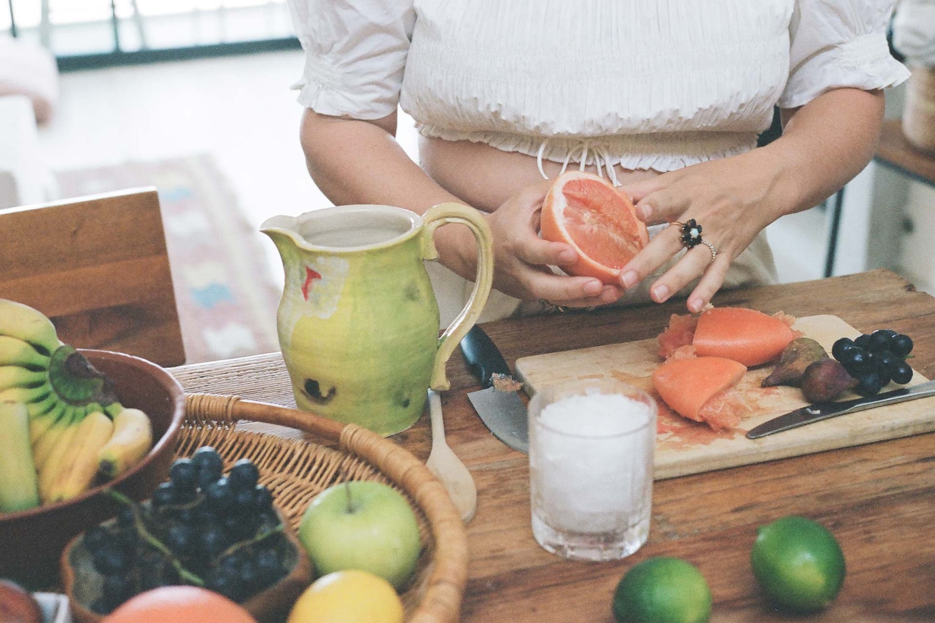 A woman wearing a white outfit prepares a fruit.