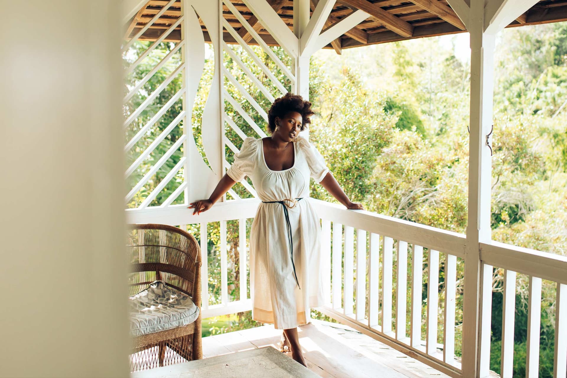 A woman wearing an all white outfit stands on an outdoor porch.