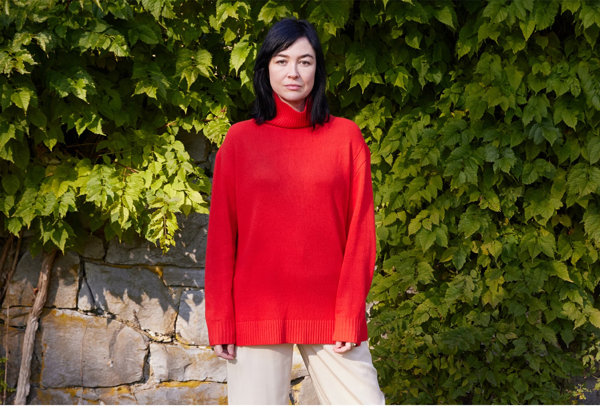 A woman wearing a red sweater stands outside.